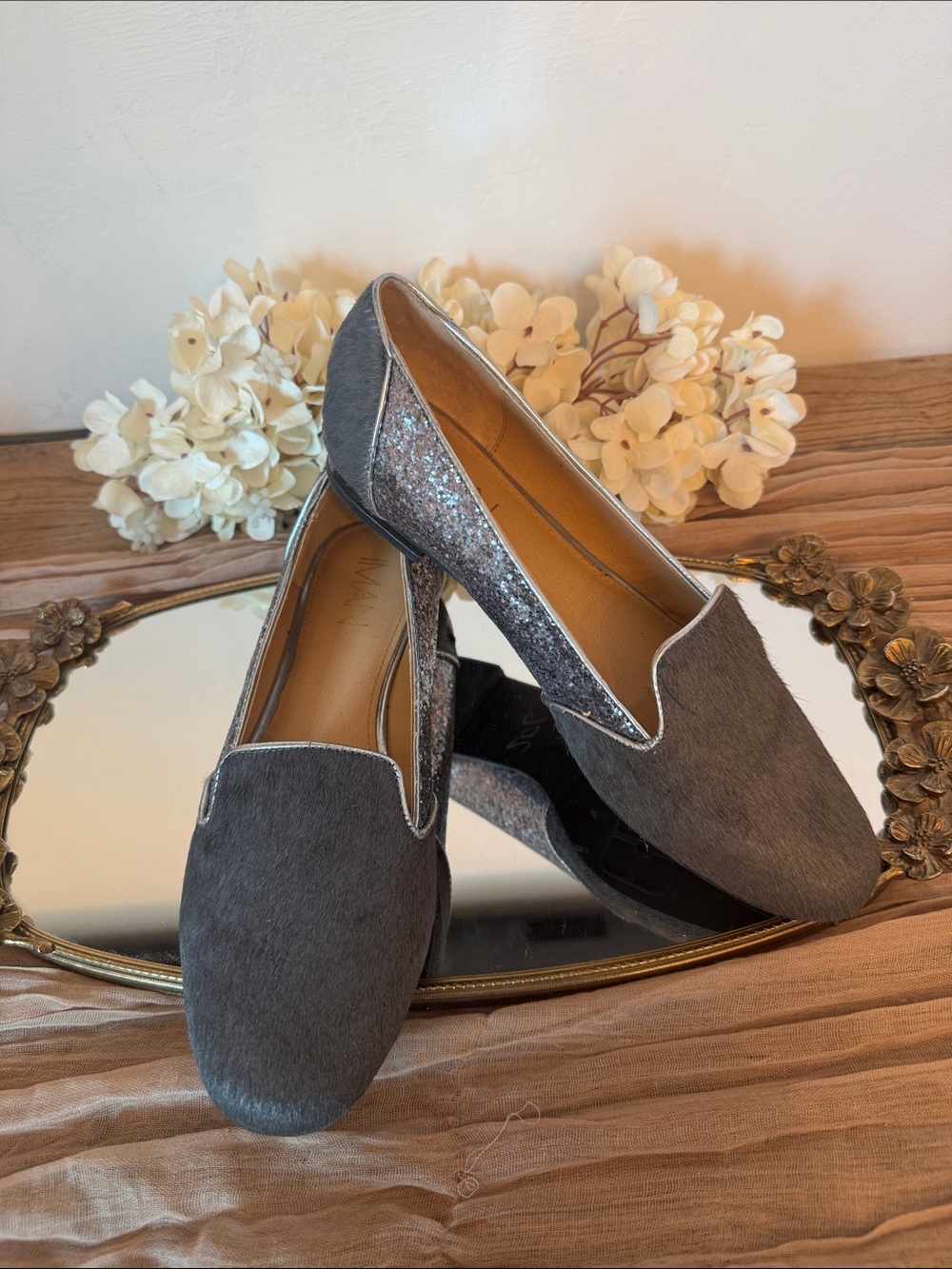 These are IMAN brand flat slip-on loafers featuring a grey calf hair upper